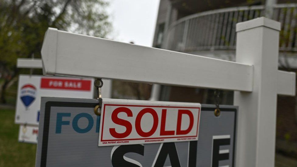 Photo of a 'Sold' sticker on a 'For Sale' sign outside a home in Canada.