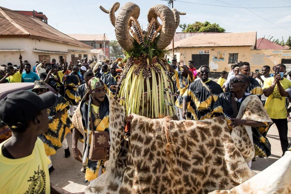 Members of the 'Ekum Baba' escort their hunting costume during the annual hunting festival in Banjul on January 2, 2023. - This hunting festival occurs every new years in Banjul. The two groups 'Ekum Baba' and 'Odilleh' come to the streets of Banjul every year to battle for the title of best animal heads,masques and costumes