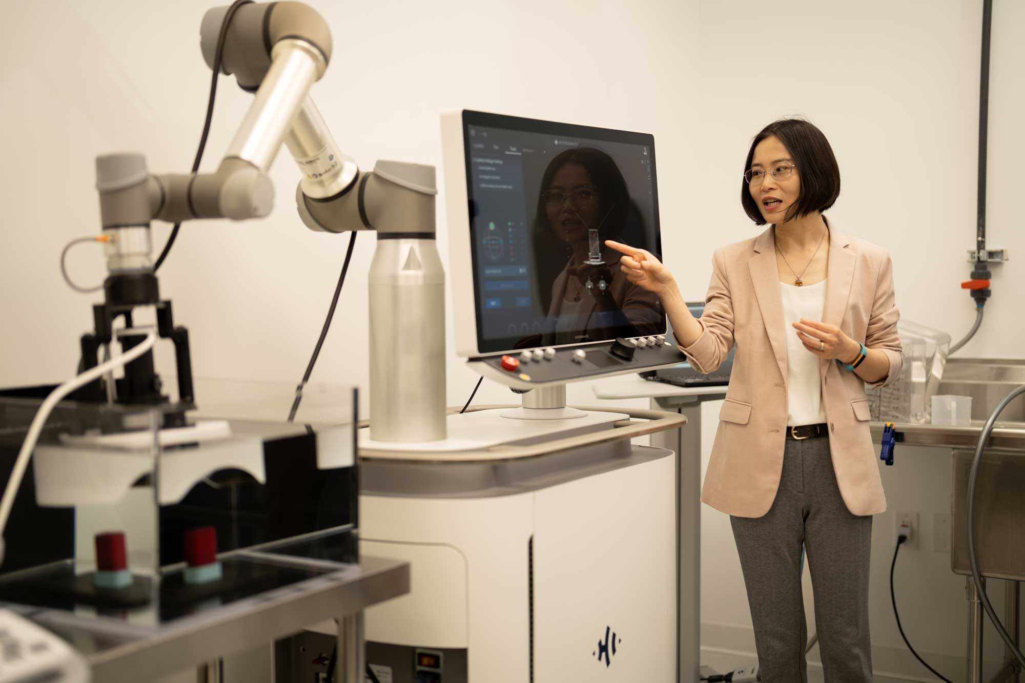Xu stands next to a computer screen showing the progress of the histotripsy treatment being used on a fake tumor in a tank of water. 