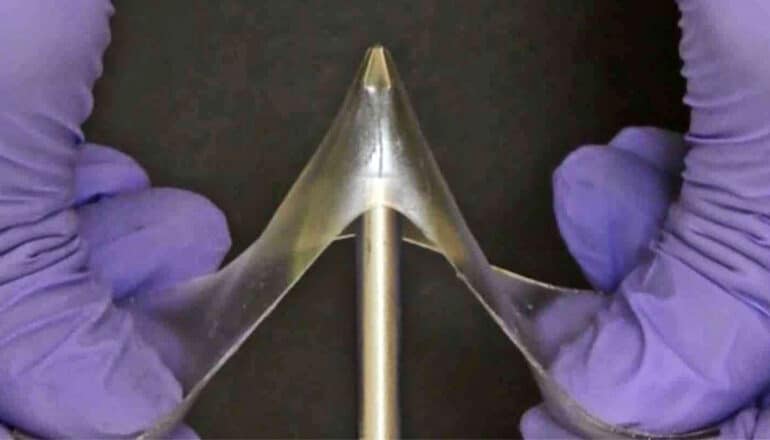 A researcher wearing purple gloves stretches the glassy gel over a nail as it deforms without breaking.